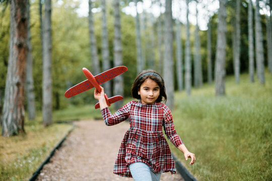 Carefree Muslim girl with toy airplane runs through park.