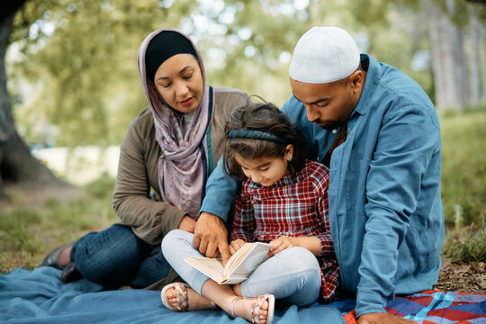 Muslim father teaches his daughter to read Koran during family picnic in nature. - Powered by Adobe
