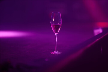 a glass of champagne stands on a stage illuminated with purple and pink lights. a glass of champagne on stage during a concert.