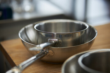 two metal frying pans on a wooden table in the kitchen, close-up