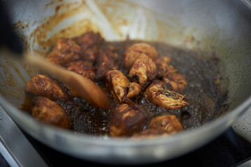the process of cooking chicken in teriyaki sauce. cooking chicken in sweet and sour sauce. chicken pieces with teriyaki sauce in a metal bowl