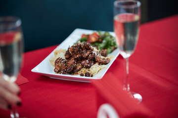served table, sweet and sour chicken with sesame seeds on a white plate and glasses of champagne