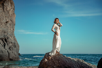 Middle aged woman looks good with blond hair, boho style in white long dress on the beach...
