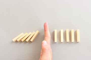 a male hand stopping the domino effect. retro style image executive and risk control concept