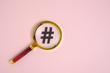 Hashtag symbol under magnifying glass, on pink background.