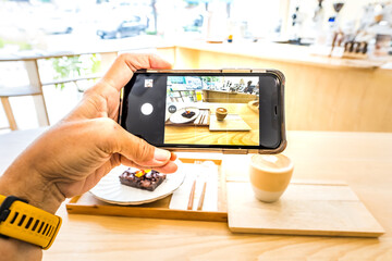 Hand holding cell phone to take photo coffee on the wooden table, top view and blurred background