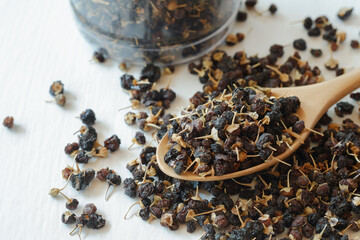 Black wolfberries or black goji berries, in a wooden spoon. Chinese herbs commonly used in...