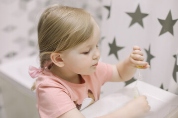 Naklejka premium portrait of a cute baby girl playing with water and soap bubbles in a bath sink at home