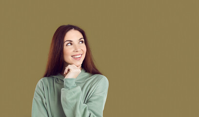 Obraz premium Smiling pensive young Caucasian woman isolated on green studio background look at blank copy space thinking. Happy female consider good sale deal or promotion discount. Copyspace. Wide.