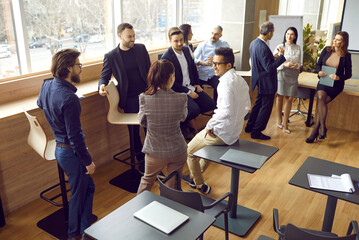 Obraz premium Nice talk. Friendly diverse employees or office workers communicating, talking, joking and sharing gossips during break. Business people communicate in modern coworking center with loft-style interior