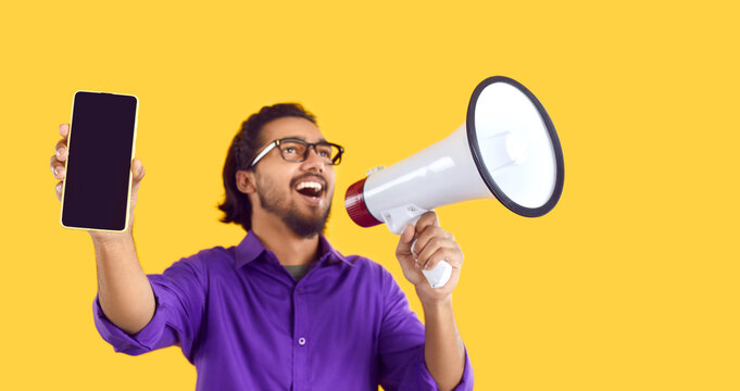 Studio shot excited young man yelling through megaphone, drawing attention to mobile with mockup copy space screen, promoting phone model, recommending Internet store sale, offering special discount