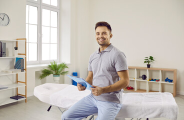 Portrait of smiling man masseur or physiotherapist in own medical office wait for client. Happy male therapist or osteopath in rehabilitation clinic on working day. Medicine and healthcare concept. - obrazy, fototapety, plakaty