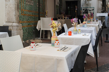 Well-served tables in a cafe (restaurant), fresh colored flowers in vases, white tablecloths, summer terrace. Holidays in Italy,