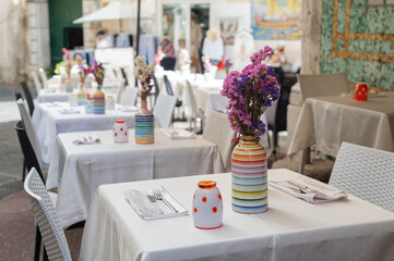 Well-served tables in a cafe (restaurant), fresh colored flowers in vases, white tablecloths, summer terrace. Holidays in Italy,