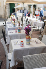Well-served tables in a cafe (restaurant), fresh colored flowers in vases, white tablecloths, summer terrace. Holidays in Italy,