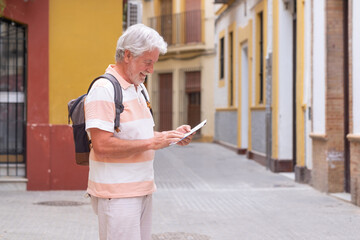 Happy senior tourist man with backpack walking in the alleys of the old town of Seville, Spain, following on the map the right direction