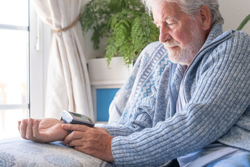 Senior bearded man using medical device to measure blood pressure, elder grandfather sitting at...