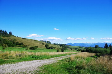 Landscape panorama shot of green meadow with path and beautiful blue sky in summer. Nature panorama with blue sky and clouds. Slovakia, Liptov-Prosiecka dolina. Enviromental concept.