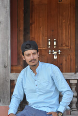 A good looking north Indian young guy with wearing cap backwards, looking at camera while sitting in temple 