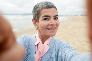 Jolly senior woman taking selfie at beach. Woman with make up taking picture of herself at sea...