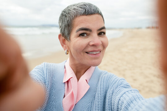 Jolly senior woman taking selfie at beach. Woman with make up taking picture of herself at sea coast. Making faces. Selfie, portrait concept