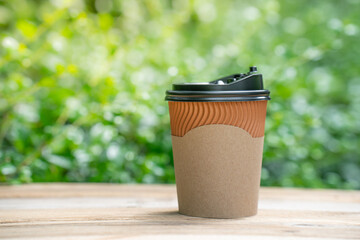 paper coffee cup on the wooden floor, green tree bokeh background.