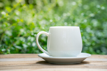 white ceramic coffee mug On the wooden floor, green tree bokeh background.