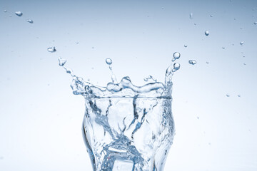 Ice cube fell into the glass of water. Water splashed from the clear glass. Fresh concept