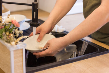 Closeup of mans hands washing dishes in kitchen sink.