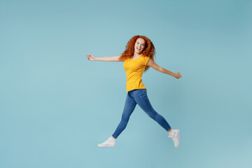 Fototapeta na wymiar Full body side view young smiling happy redhead woman 20s wearing yellow t-shirt jump high walk go look camera isolated on plain light pastel blue background studio portrait. People lifestyle concept.