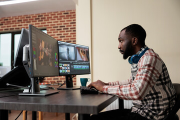 Fototapeta na wymiar Video production house employee sitting at multi monitor workstation while editing movie frames using advanced software. African american graphic footage editor enhancing project quality.