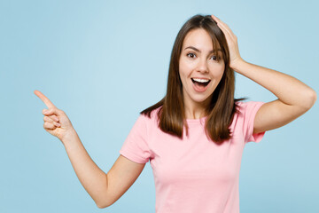 Fototapeta premium Young surprised amazed woman 20s in pink t-shirt point index finger aside on workspace area mock up copy space isolated on pastel plain light blue background studio portrait. People lifestyle concept.