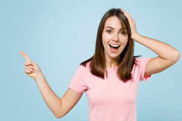 Young surprised amazed woman 20s in pink t-shirt point index finger aside on workspace area mock up copy space isolated on pastel plain light blue background studio portrait. People lifestyle concept.