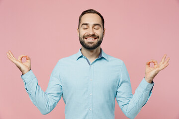 Fototapeta premium Young smiling spiritual tranquil fun man 20s wear classic blue shirt hold spreading hands in yoga om aum gesture relax meditate try to calm down isolated on plain pastel light pink background studio