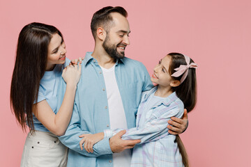 Young smiling parents mom dad with child kid daughter teen girl in blue clothes hugging each other look to each other isolated on plain pastel pink background. Family day parenthood childhood concept.