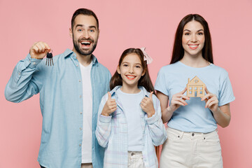 Young happy excited cool fun smiling parents mom dad with child kid daughter teen girl in blue clothes hold keys wooden house mockup isolated on plain pastel light pink background. Family day concept.