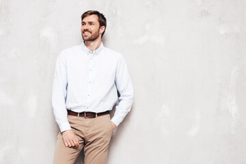 Portrait of handsome smiling model. Sexy stylish man dressed in shirt and trousers. Fashion hipster male posing near grey wall in studio. Isolated.