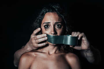 Woman being silenced by her partner. Man's hands putting on duct tape on her mouth