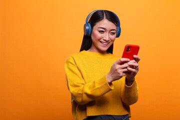 Calm peaceful young adult woman wearing headphones while using smartphone to enjoy funny online...