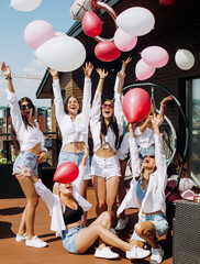 Happy girls dancing and having fun on the roof at home. Girlfriends throw helium balls up. Maiden...