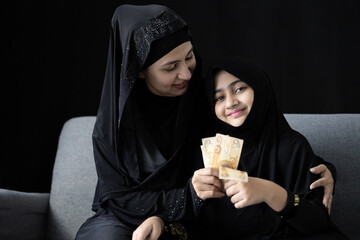 muslim woman or mother giving cash money to her daughter on black background