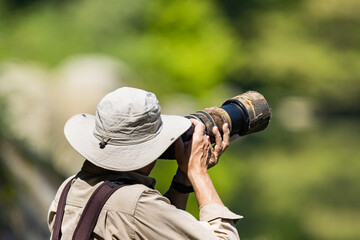 Wildlife photographer using a telephoto lens with camouflage coating, selective focus on the cap.