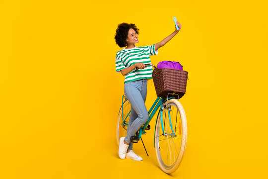 Full body photo of nice young lady drive bicycle do selfie wear t-shirt jeans footwear bag isolated on yellow background