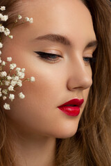 Fototapeta premium Close up portrait of a face with beautiful skin and evening makeup, eyeliner and long eyelashes, puffy red lips and white flowers. Fashion photography. Cosmetology and spa. Freshness of spring