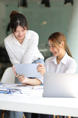 Businesswoman colleagues in the office discussing work and planning projects together on a tablet at their desk.