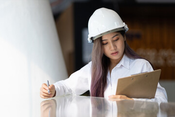 Young architect or engineer working in an office is writing a note on the design of a building model on a notepad.