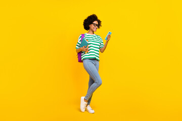 Fototapeta na wymiar Full body photo of cute young lady look telephone hold book wear glasses t-shirt bag jeans sneakers isolated on yellow background