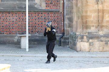 Człowiek z karabinem kałasznikow w czarnym ubiorze idzie ulicą. - obrazy, fototapety, plakaty