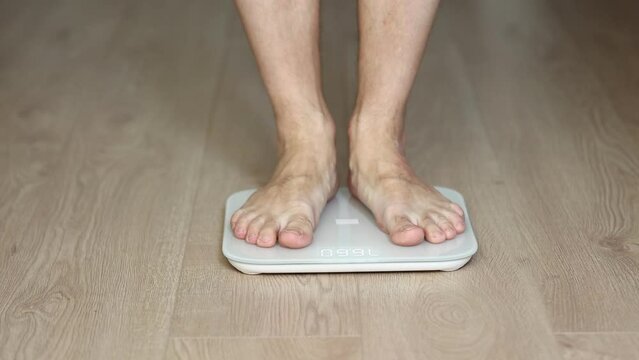 Man walking on scales measure weight. male wal checking BMI weight loss. human barefoot measuring body fat overweight. Guy legs step on bathroom scale.