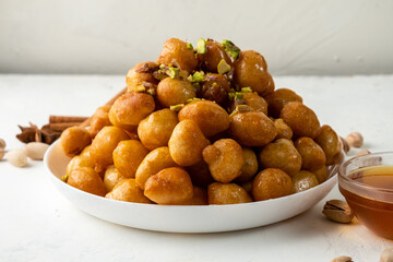 luqaimat or lokma sweet arabic fried dough dessert with sweet syrup in white plate on light background.